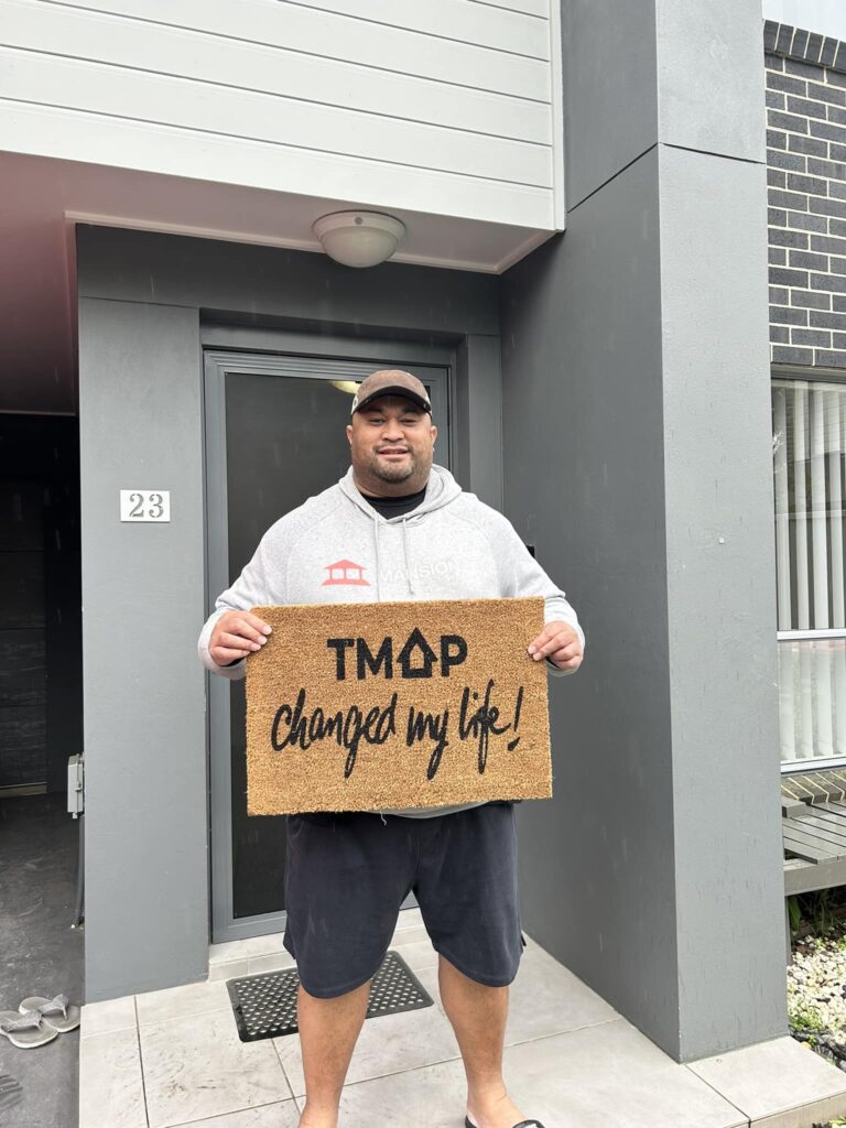 A TMAP family holding their TMAP doormat