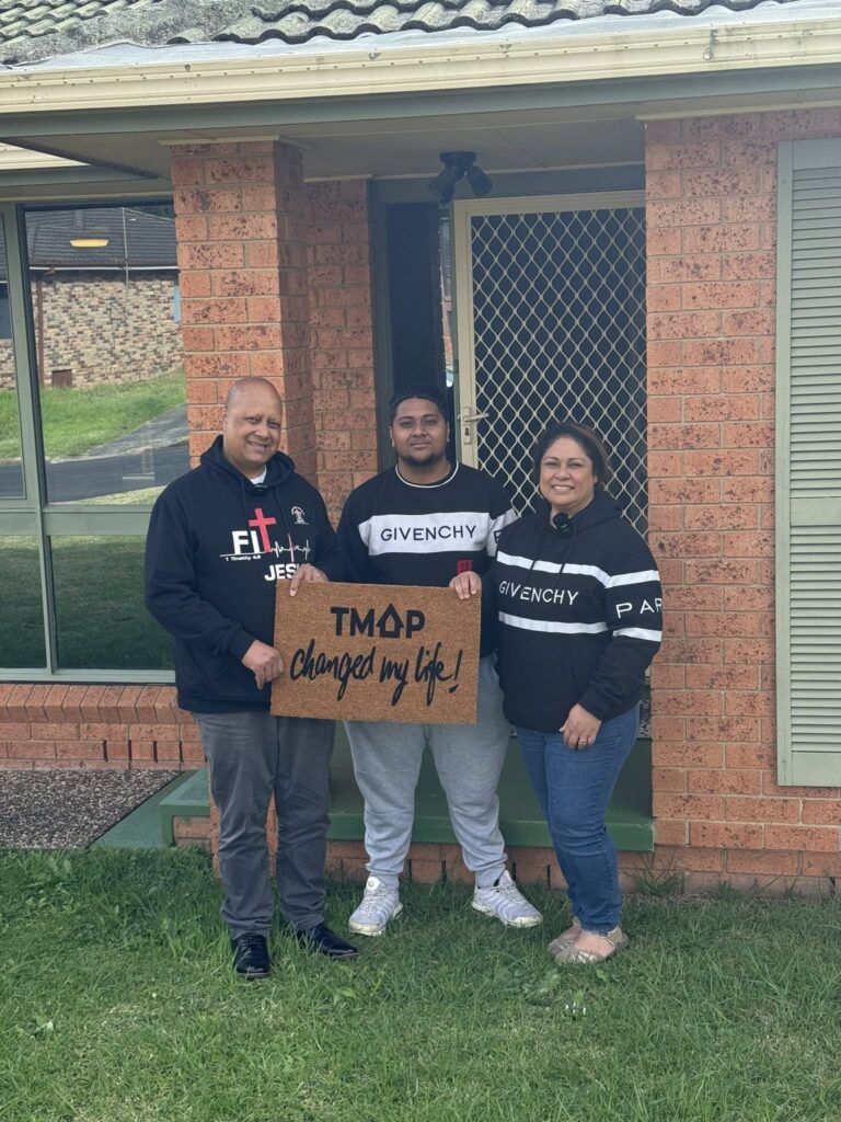A TMAP family holding their TMAP doormat