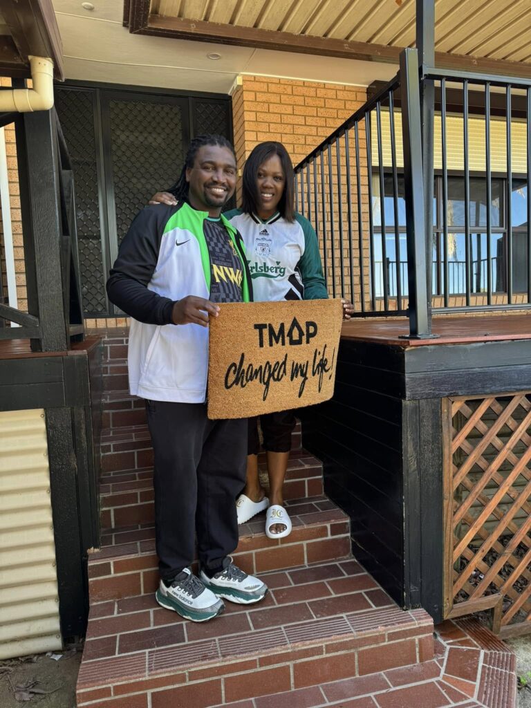 A TMAP family holding their TMAP doormat