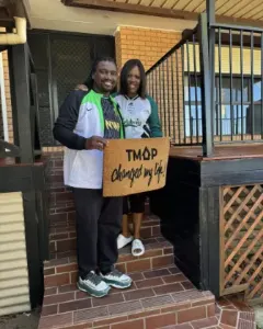 A TMAP family holding their TMAP doormat
